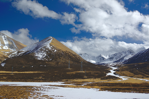snow mountain in Tibet, China, with power transmission towers in the wild valley.