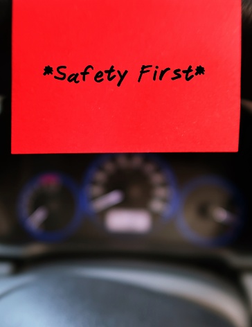 Red sticky note with text written SAFETY FIRST , on the car steering wheel , to remind driver to drive carefully and with awareness