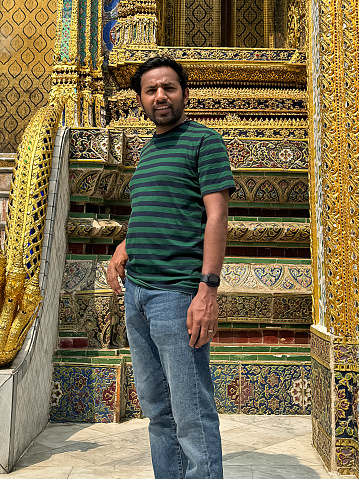 Stock photo showing close-up view of an Indian tourist standing outside the ornately, decorated walls of Wat Phra Kaeo (Royal Grand Palace), Bangkok, Thailand.