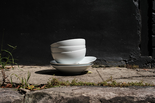 Stack of saucers and bowls on the side of a road in front of a black wall.