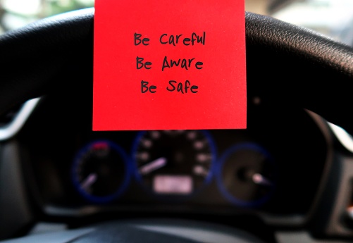 Red sticky note with text written BE CAREFUL BE AWARE BE SAFE , on the car steering wheel , to remind driver to drive carefully