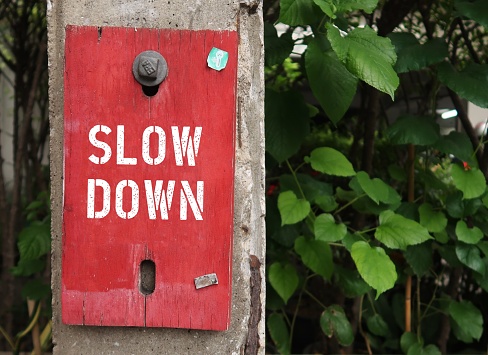 Red sign board with text SLOW DOWN, means  to slow down speed when you find yourself feeling rushed, busy or overwhelmed, find balance in life