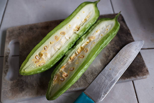 A bitter melon vegetable cut in half with a knife on a cutting board, stock photo.