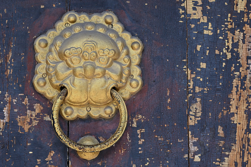 Lion door knocker in gold on a faded wooden door offers protection to those within