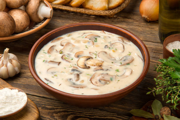 Cream of mushroom soup in a terracotta clay bowl with ingredients on a wooden rustic table. stock photo