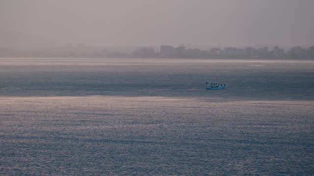Boat going forward in the middle of the sea with the city in the background on the sea at sunset.