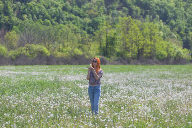 Woman enjoy at meadow full of dandelion seed on sunny springtime day in nature