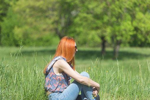 Woman sitting and relaxing at green grass meadow in springtime