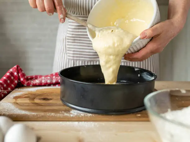 Woman pouring batter or dough into a round baking pan in the kitchen for making dough or batter.
