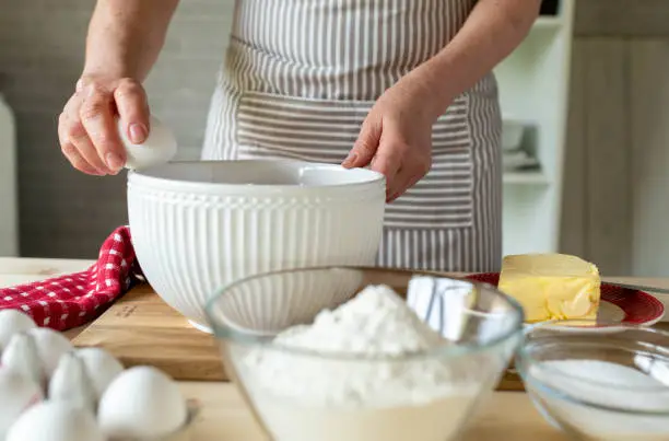 Woman is cracking an egg on the edge of a bowl for making dough