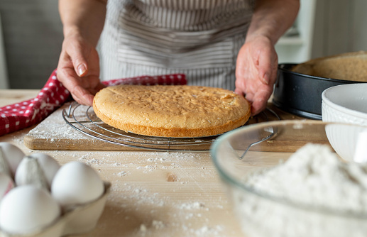 Placing a fresh baked cake base on a cooling rack by woman´s hands in the kitchen. Front view