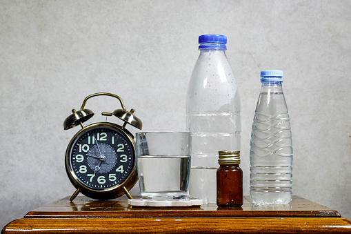 alarm clock with glass of water and medicament bottle on wood table