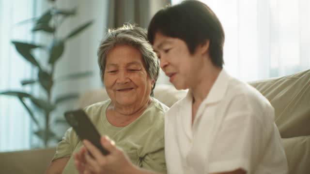 Two elderly woman relax watching entertainment on smartphone.
