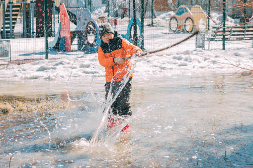 Winter's Last Dance - A young child splashes through the melting remnants of winter, shovel in hand, embodying the joyful transition to warmer days