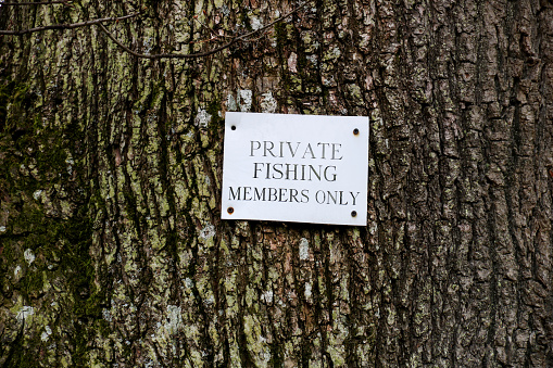 Private fishing sign nailed to a tree trunk in a countryside location