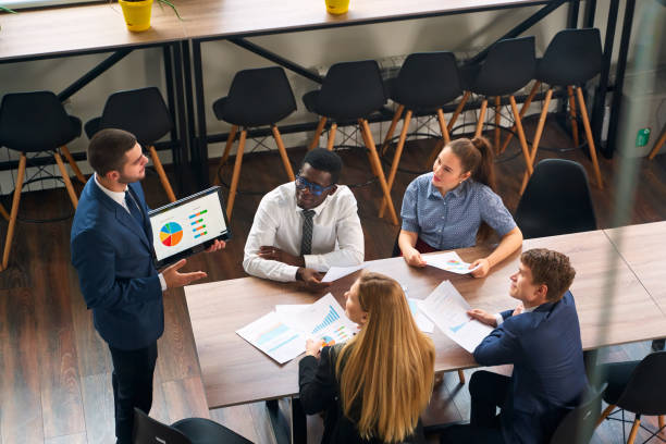 istock Arabic executive shares data on tablet with multiethnic team in modern office. Colleagues discuss strategy, graphs. Engaged diverse group analyzes market, plans goals at corporate meeting. 2148602900