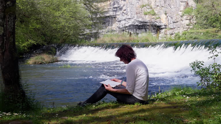 SLO MO Senior woman relaxing by reading a book next to small waterfall.