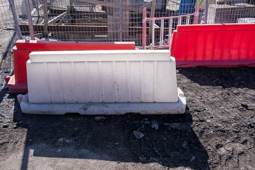 Construction hole is surrounded by white and red plastic barriers and a metal fence. Construction and engineering work on laying underground communications