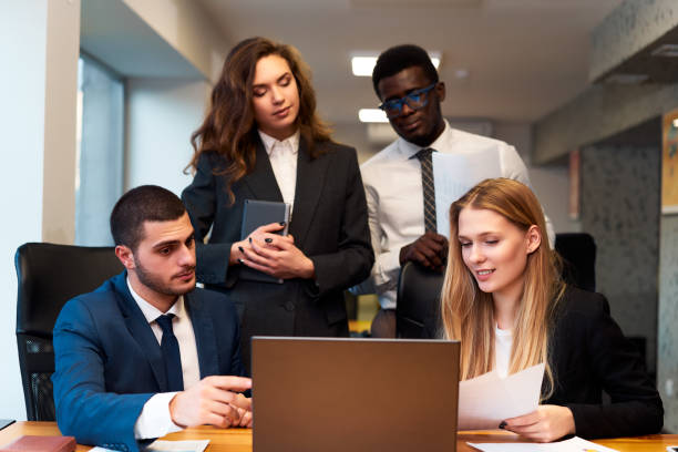 istock Multiracial business team collaborates in a modern office. African, Caucasian, Arabic execs engage in project discussion. Woman with tablet, colleagues review data on laptop for corporate success. 2148604076