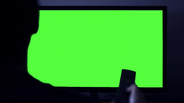 Silhouette of A Man Pointing Remote Control on Smart TV Green Screen at Night. Close up. 4K Resolution.