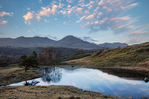 Beautiful sunset landscape image of Kelly Hall Tarn in Lake District with Old Man of Coniston in background