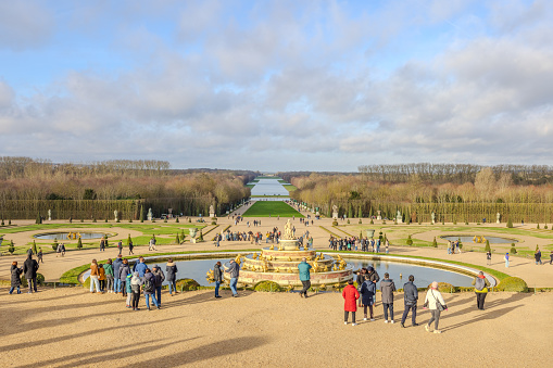 Chateau de Versailles, Versailles, France - December 28, 2023:  Tourists seen in the Gardens of the Chateau de Versailles in a cloudy morning.  The symmetry of Latona's Pool and Parterre in the foreground all the way back to as far as can be observed.  HDR encoded.