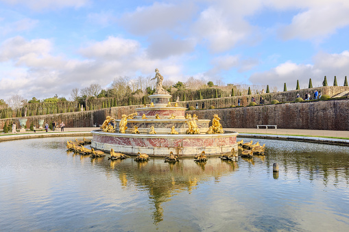 Horizontal closeup of the exterior gold-painted fence and the rear view of a sculpture mounted on a plinth in the grounds of the Palace of Versailles