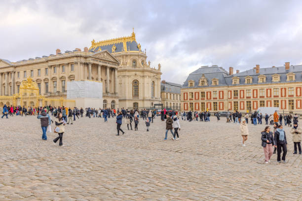 Paris, France - January 11, 2010: Gardens of Versailles. Statue on the Water Parterre at sunset. The palace facade and tourists enjoying can be seen in the background. This is one of the most visited monuments in France.