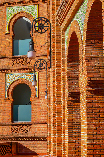 Closeup of exterior brick walls with pillars and arched windows, neo Mudejar style Las Ventas bullring, hanging lamps, sunny day in Madrid, Spain