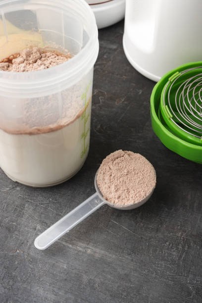 istock Whey protein powder with a chocolate flavor in a plastic measuring spoon, shaker with a milk and bananas on a dark background, process of making protein shake drink 2148609272