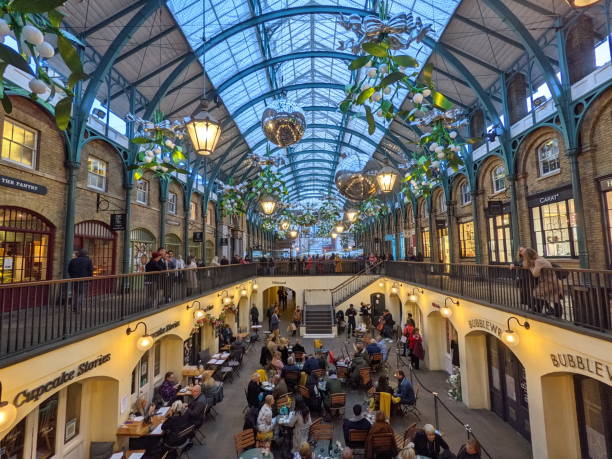 People enjoying al fresco dining at Covent Garden Market, London, on a sunny day, socializing at outdoor tables amid vibrant urban streets and historic architecture.