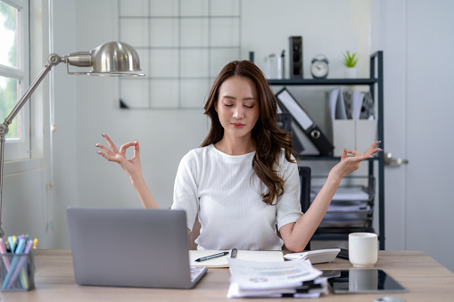 Businesswoman practicing mindfulness meditation to de-stress and refocus at her home office desk.