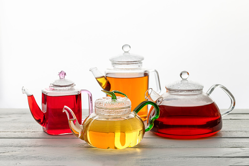 Different type og tea in different glass teapots on the white wooden table