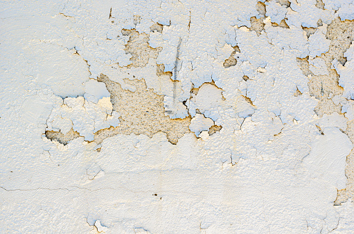 Close-up of white peeling paint on an exterior stucco wall of a vintage building.