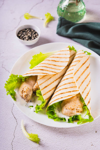 Grilled chicken fillet wrapped in tortilla with lettuce and sauce on a plate vertical view