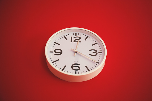 A simplistic white clock with bold numerals against a vibrant red backdrop