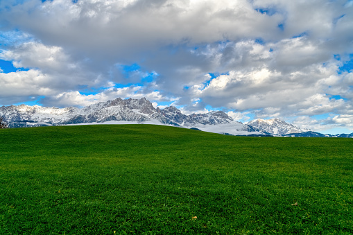 a beautiful alpine landscape near Saalfelden in Salzburger Land in Austria. rural scene with a green meadow, snowcoverd mountains and cloudy sky.