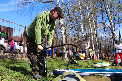 Participant of the Ryazan Sea festival. A man pumps up a SUP board using a hand pump. Sunny day, Ryazan city, Forest Park, April 13, 2024