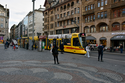 Basel, Switzerland - March 21, 2024: Basel City Public Transportation Tram, Land Vehicle, Building Exterior, People Walking, Shopping, Waiting For Tram, Eating And Drinking In A Restaurant Scene And More