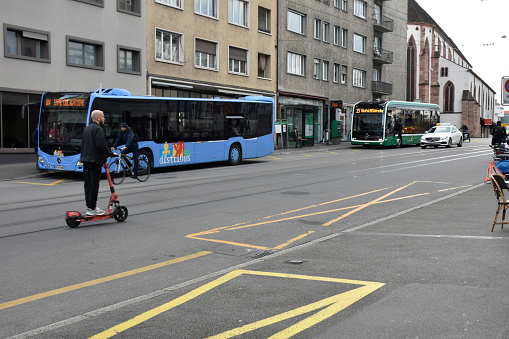 Basel, Switzerland - March 21, 2024: Basel City Public Transportation Bus, Taxi, Land Vehicle, Building Exterior, People Riding Electric Scooter, Walking, Riding Bicycle Scene And More