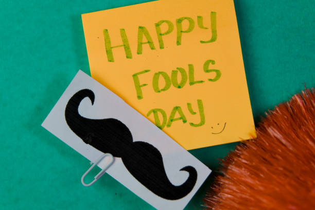 Happy Fools Day message on sticky note with mustache on green background