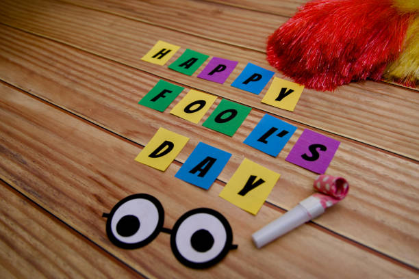 Happy Fools Day text on colorful sticky notes with accessories on wooden background