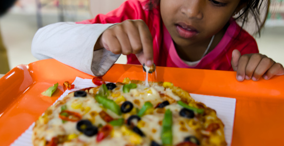 A close-up photo of a  young girl with a look of pure enjoyment on her face as she takes a bite of a delicious pizza slice