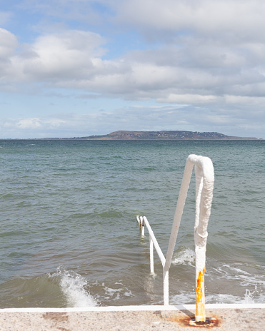Submerged handrails and steps in the sea at Seapoint in Ireland. Howth is in the background