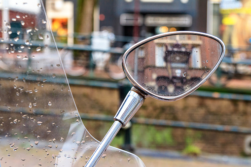 Close-up view of the rearview mirror of a scooter with the inscription: objects in the mirror are closer than they appear. On a rainy day in the historical center of Amsterdam