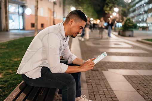 Seated on a city bench, a businessman navigates through charts and graphs on his digital tablet, orchestrating success in the palm of his hand.