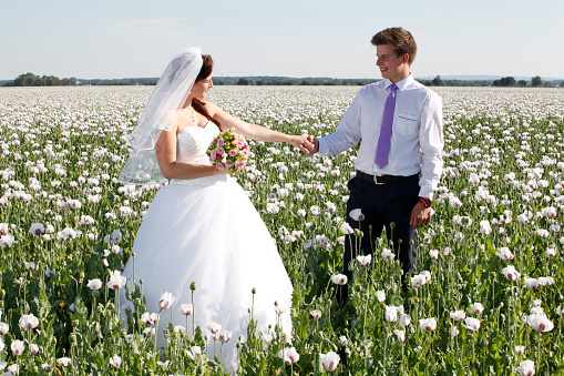 Happy couple standing together after the wedding ceremony standing in a field full of white poppies.