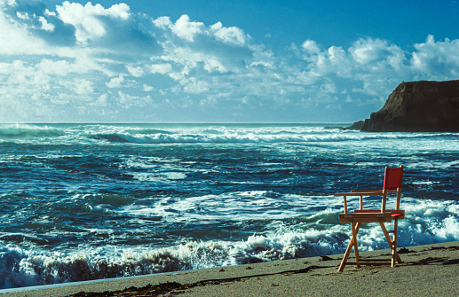 Ocean view of a remote beach where turbulent waves are crashing near an unoccupied beach chair on the shore.\n\nTaken in Davenport Beach, California