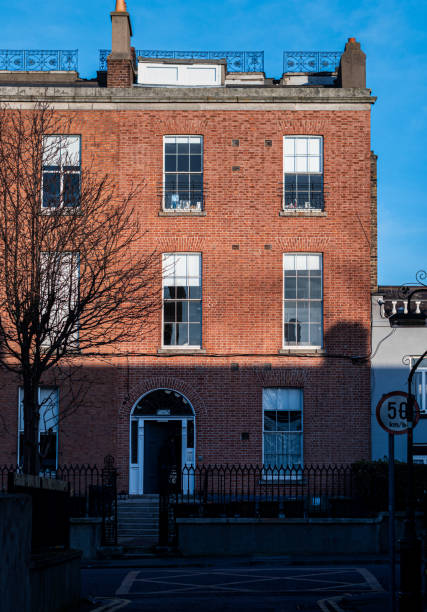 Dublin, Ireland - 02/05/2023: facade of an old, red brick building with shadow on the bottom part of the house. The blue sky is visible in the background.