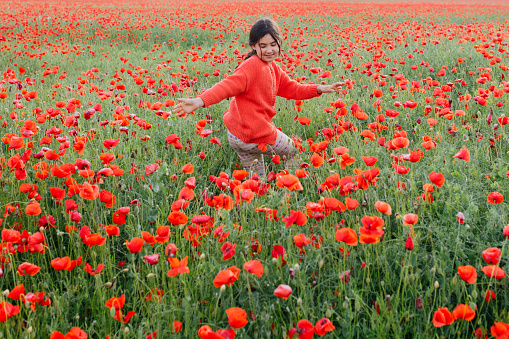 wide angle view of child in red clothes dancing in the field of poppies